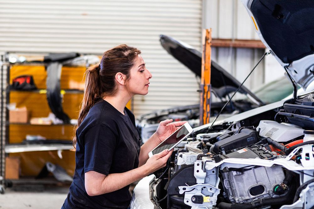 ميكانيكي يفحص حجرة المحرك في سيارة مفتوحة الغطاء، مناسب لموضوع أعطال بلف الحرارة ونظام التبريد